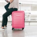 Long flight in economy photo. Picture of a lady sitting on a pink carry on suitcase.