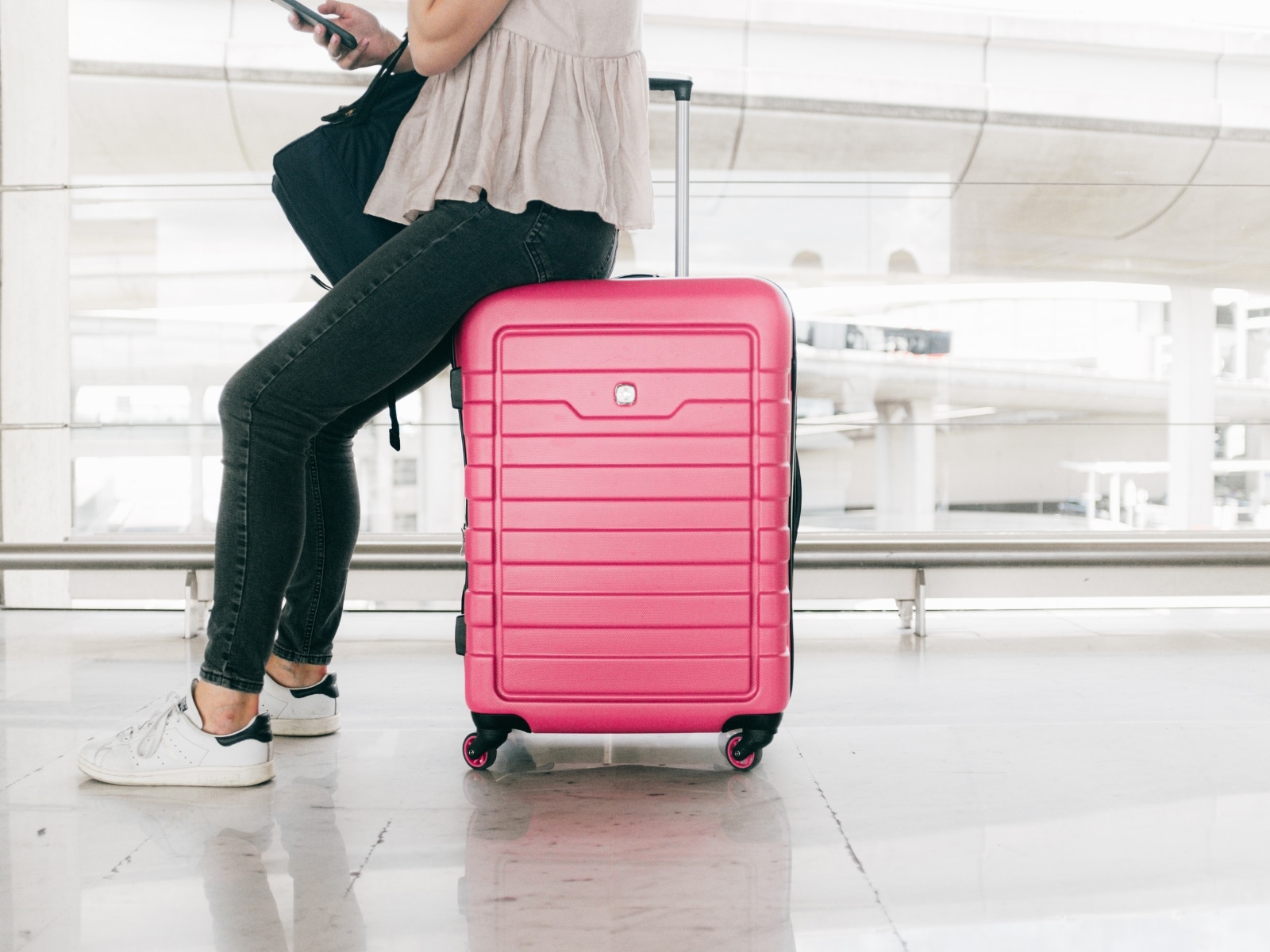 Long flight in economy photo. Picture of a lady sitting on a pink carry on suitcase.