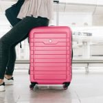 Picture of a lady sitting on a pink carry on suitcase.