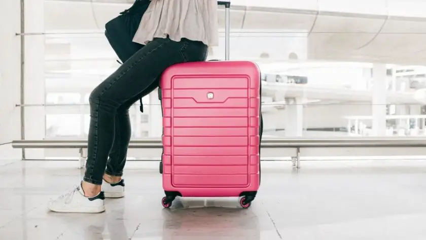 Picture of a lady sitting on a pink carry on suitcase.