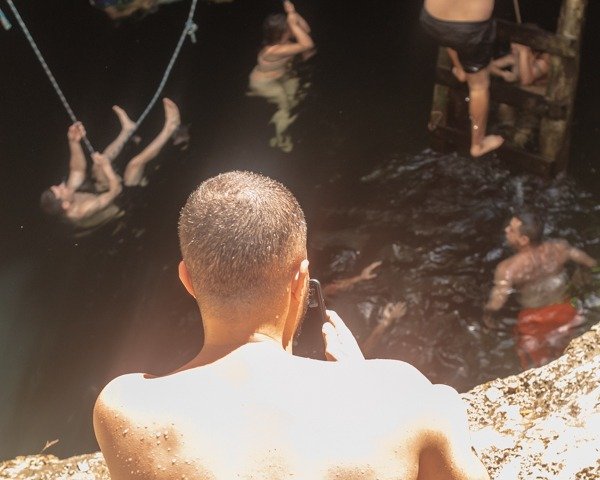 Man looking into Cenote calavera and below a crowd of people swimming