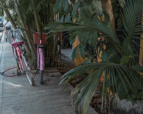 Colorful pink beach cruisers parked outside of a yellow building in Tulum town. 