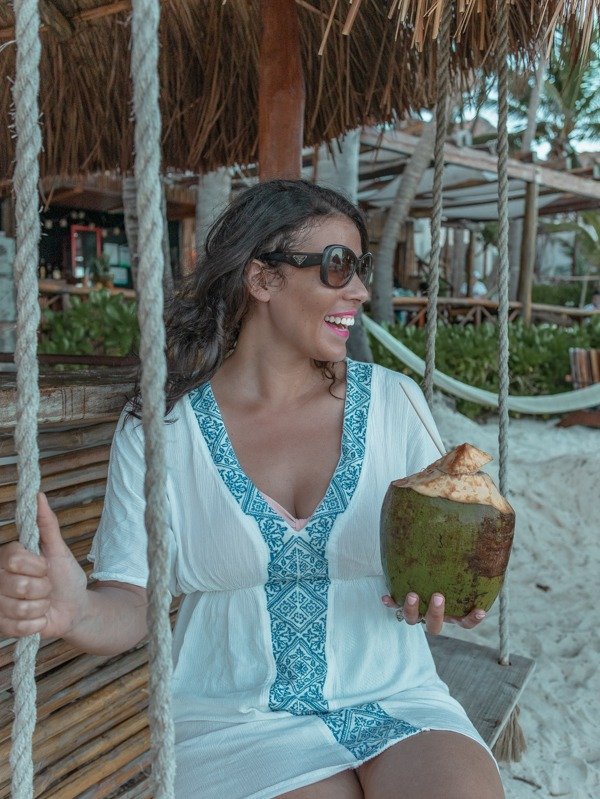 Me on a swinging near beach hut holding a coconut on one of the Tulum beaches