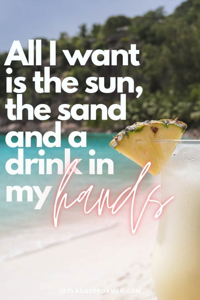 Frozen cocktail sitting on the sand on a beautiful tropical island on a sunny day with text that says "All I want is the sun, the sand and a drink in my hands.