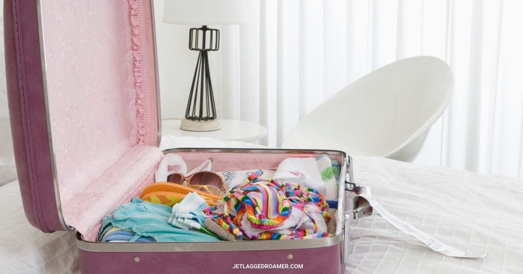 Pink suitcase on top of a bed in a bedroom that is completely white. 