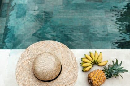 Summer captions picture of a sun hat, bananas, and a pineapple next to a clear water pool.