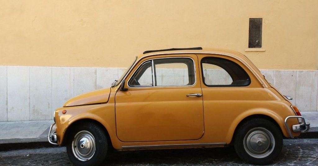 Travel expressions photo. Old yellow Fiat 500 parked on a charming European street.