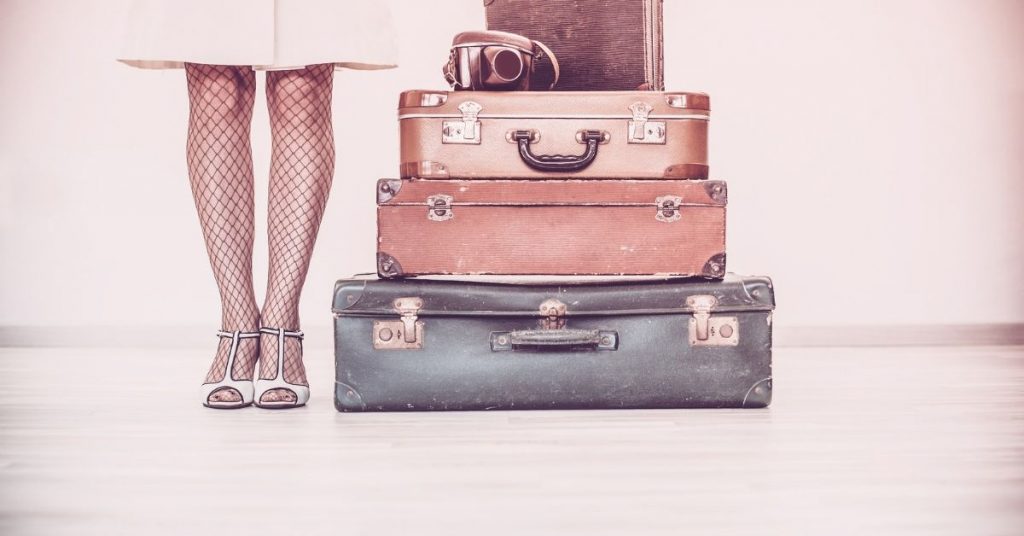 Woman dressed retro with old but stylish suitcases next to her for a travel phases photo. 