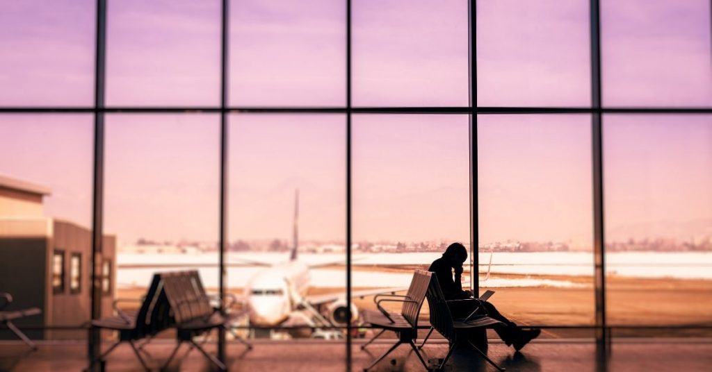 Photo for travel expressions for the airport. Sunset approaching through the window at an airport with the man sitting at the gate on his computer. 