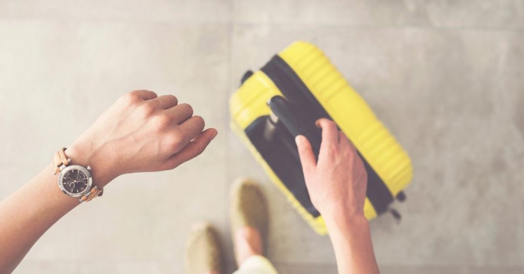 Useful expressions for customs photo of a woman looking down at her watching and holding her yellow carry on suitcase.