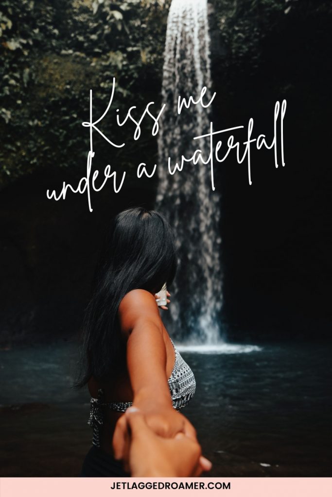 Waterfall caption for Instagram that says “Kiss me under a waterfall.” Image of a woman holding someones hand and looking at a waterfall. 