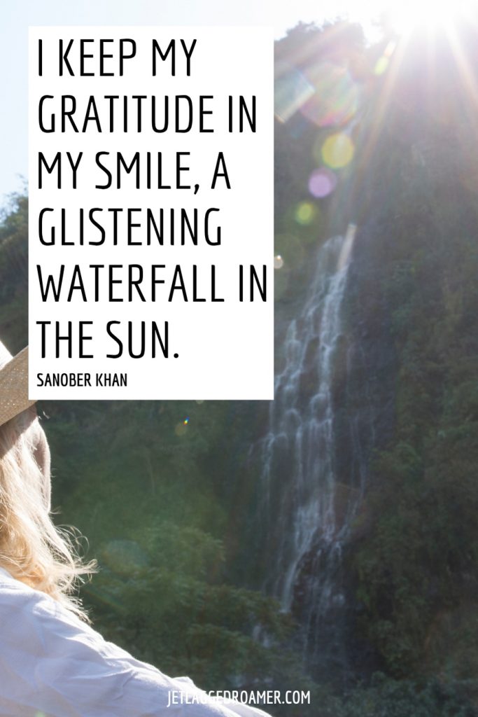 Woman staring at a waterfall a far off on a sunny day. Text is a waterfall quote that says “I keep my gratitude in my smile, a glistening waterfall in the sun" by Sanober Khan.