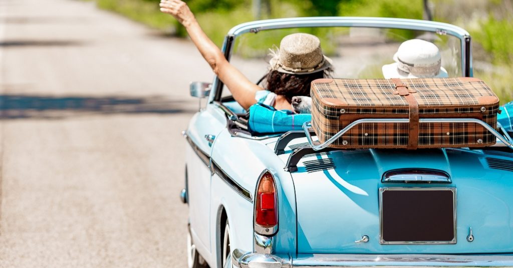 Two girlfriends driving an old convertible down a road on a sunny day. 