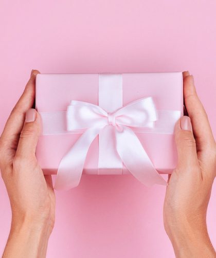 Gift for travel lovers photo os a woman holding a gift with pink wrapping paper and a white bow.