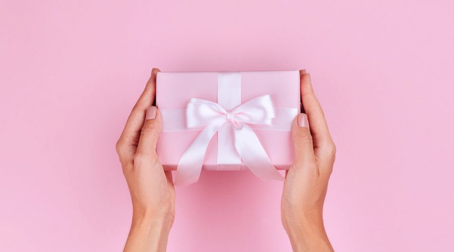 Gift for travel lovers photo os a woman holding a gift with pink wrapping paper and a white bow.