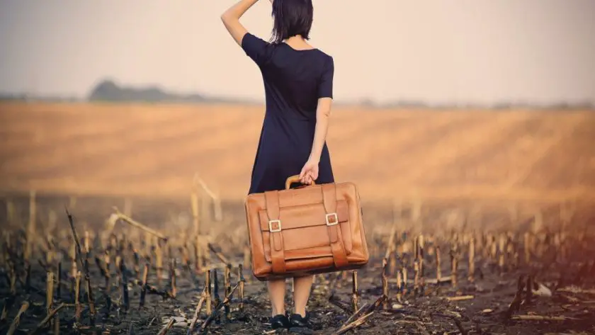 Captions for travel photo of a woman holding a suitcase in an open field alone.