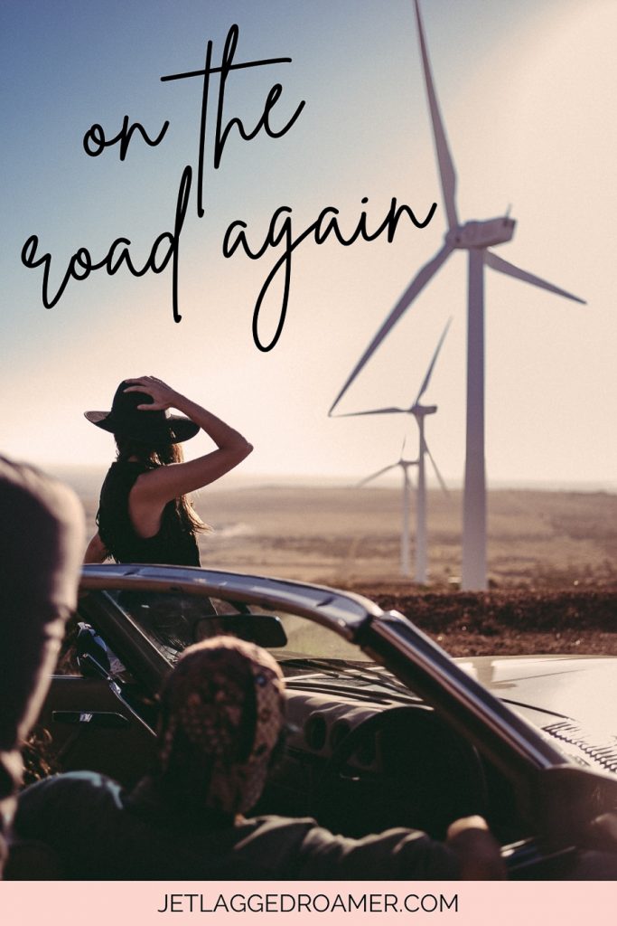 Road trip caption that reads on the road again. Couple in a car looking at windmills. 