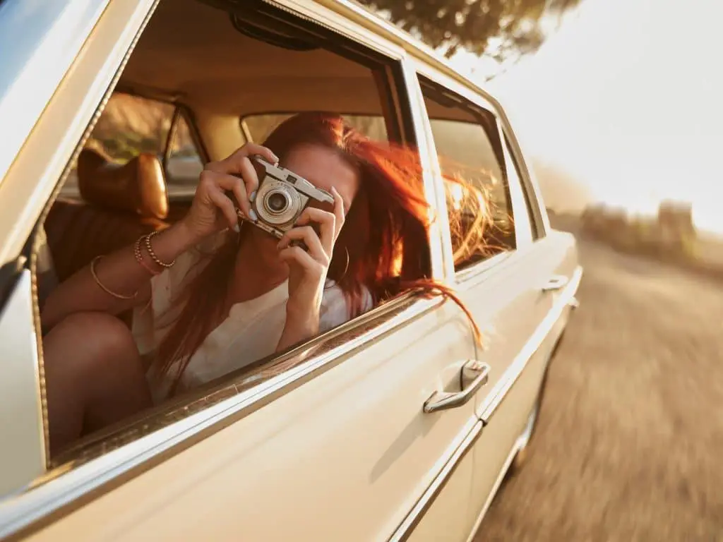 Road trip Instagram captions photo of a woman in a car taking a photo. 