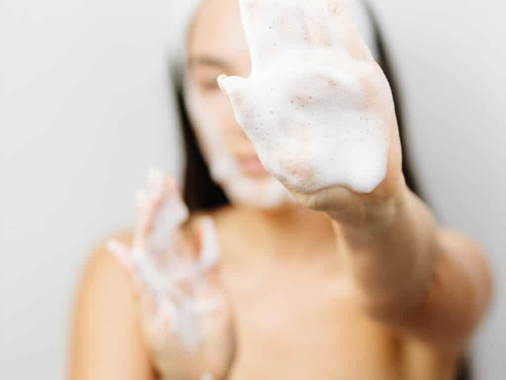 Take care of your skin while traveling photo of a woman with facial cleanser on her hands. 