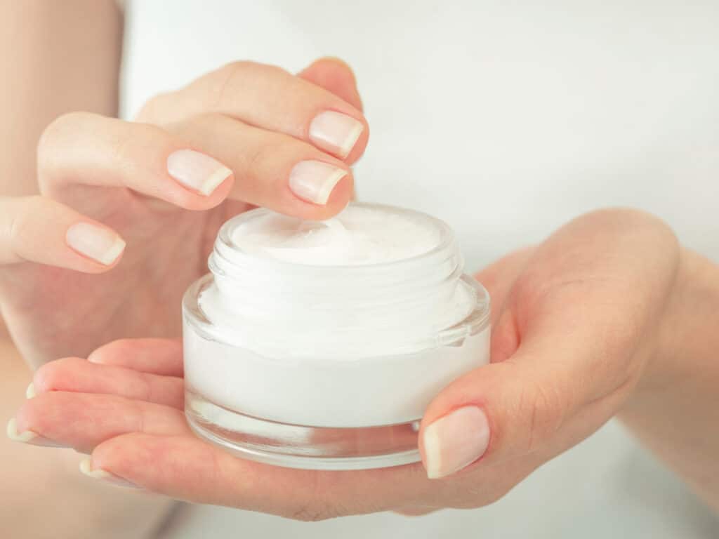 Woman holding moisturizer a must in your skin care travel kit. 