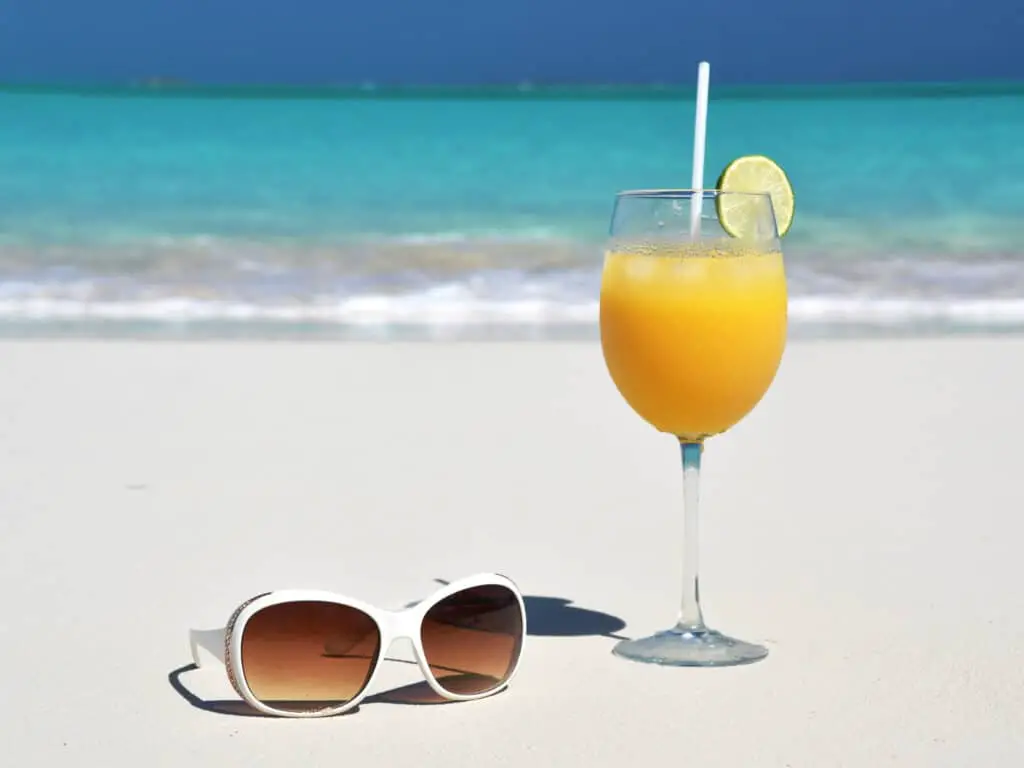Funny Bahamas captions photo of a cocktail and sunglasses on a beach in Bahamas. 